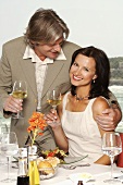 Couple with wine glasses at laid table by sea