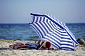 Blau-weisser Sonnenschirm und einige Kissen am Strand