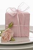 Gift in pink wrapping paper and rose on a plate