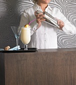 Frau mixt Drink mit Cocktailshaker, Pina Colada auf Tablett