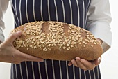 Woman holding a loaf of oat bread in both hands