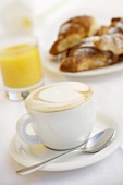 A cup of cappuccino, orange juice and brioches