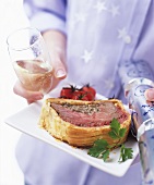 Woman carrying plate of beef Wellington, sparkling wine & cracker