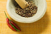 Szechuan pepper in mortar, chili peppers beside it