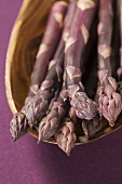 Purple asparagus in wooden bowl