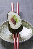 A maki sushi with tuna and cucumber on chopsticks