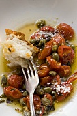 Roasted tomatoes with capers, white bread on fork