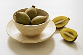 Three kiwi fruits in bowl, one halved beside it
