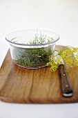 Dill in glass bowl and dill flowers on chopping board