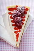 Piece of cheesecake with raspberries & icing sugar on napkin