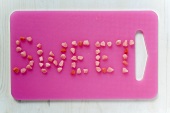 Schriftzug 'Sweet' aus Zuckerbonbons auf rosa Schneidebrett
