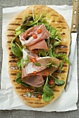 Pizza bread topped with Parma ham, herbs and chilli rings