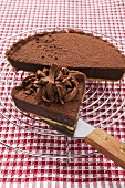 Chocolate tart on cake rack and piece on cake server