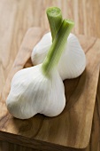 Two fresh garlic bulbs on wooden chopping board