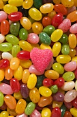Bunte Jelly Beans und ein rosa Zuckerherz (bildfüllend)