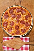 Whole pepperoni pizza, server on napkin beside it