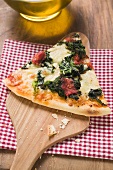 Slice of spinach, tomato and cheese pizza on server