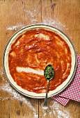 Pizza base with tomato sauce and spoonful of oregano