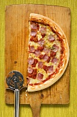 Half a ham, cheese and tomato pizza on chopping board