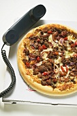 Mince and onion pizza on pizza box with telephone handset