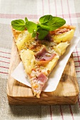 Slice of Hawaiian pizza with fresh oregano on chopping board
