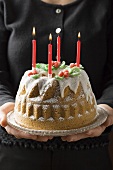 Woman serving walnut gugelhupf with four burning candles