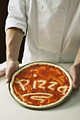 Pizzateig, mit Tomatensauce bestrichen und Schriftzug Pizza