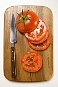 Tomato slices and knife on chopping board (overhead view)