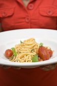 Woman holding plate of spaghetti with tomatoes and basil