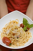 Hands holding plate of spaghetti with Parmesan and basil