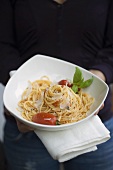 Person hält Teller Spaghetti mit Parmesan und Basilikum
