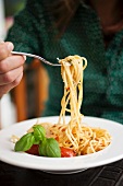 Woman eating spaghetti with tomatoes and basil