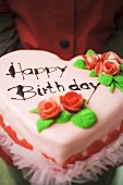 Person holding heart-shaped birthday cake with marzipan roses