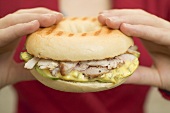 Hands holding bagel with pork fillet & honey mustard relish