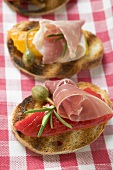 Several crostini with raw ham, peppers and giant capers