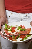 Person holding dish of tomatoes with mozzarella and basil