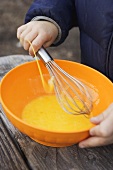 Child beating egg yolks with whisk