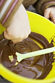 Child's hand reaching into chocolate mixture in yellow bowl