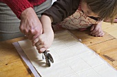 Mother and child cutting puff pastry with pastry wheel