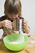 Child sieving flour into a bowl