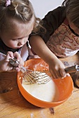 Two children stirring cake mixture with whisks