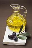 Olive sprig with black olives, carafe of olive oil behind