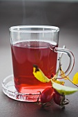 Rose hip tea in glass cup, fresh rose hips beside it