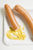 Frankfurters, partly eaten, with mustard on paper plate
