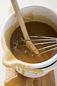 Gravy in an enamel jug with wooden spoon and whisk