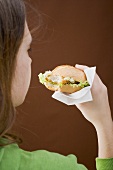 Girl eating a breaded escalope in a bread roll