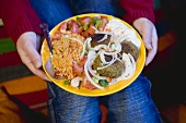 Person holding falafel with accompaniments (N. Africa)