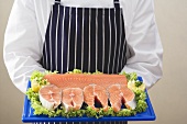 Person holding various cuts of salmon on chopping board