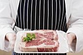 Person holding two sirloin steaks on tray