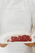 Person holding sirloin steak on tray
